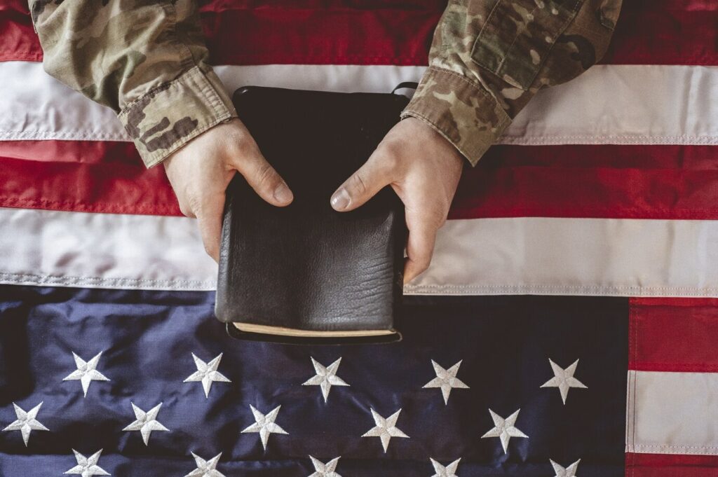 Hands holding a Bible over an American flag.